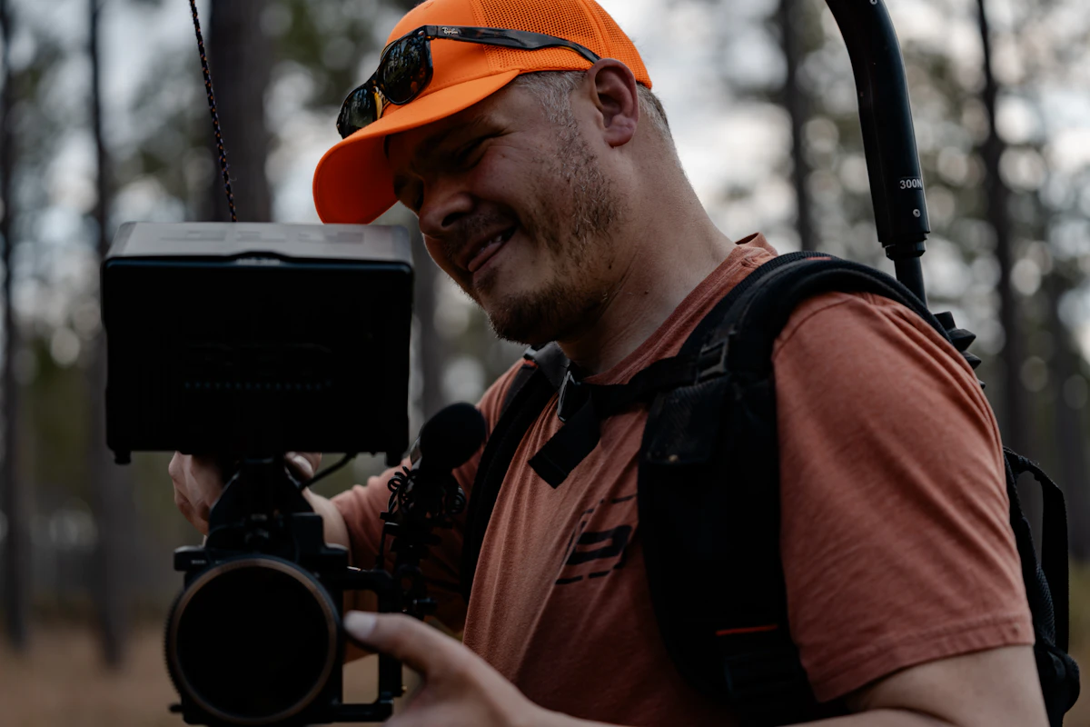 Camera operator in an orange cap reviewing a cinema camera monitor during an outdoor shoot